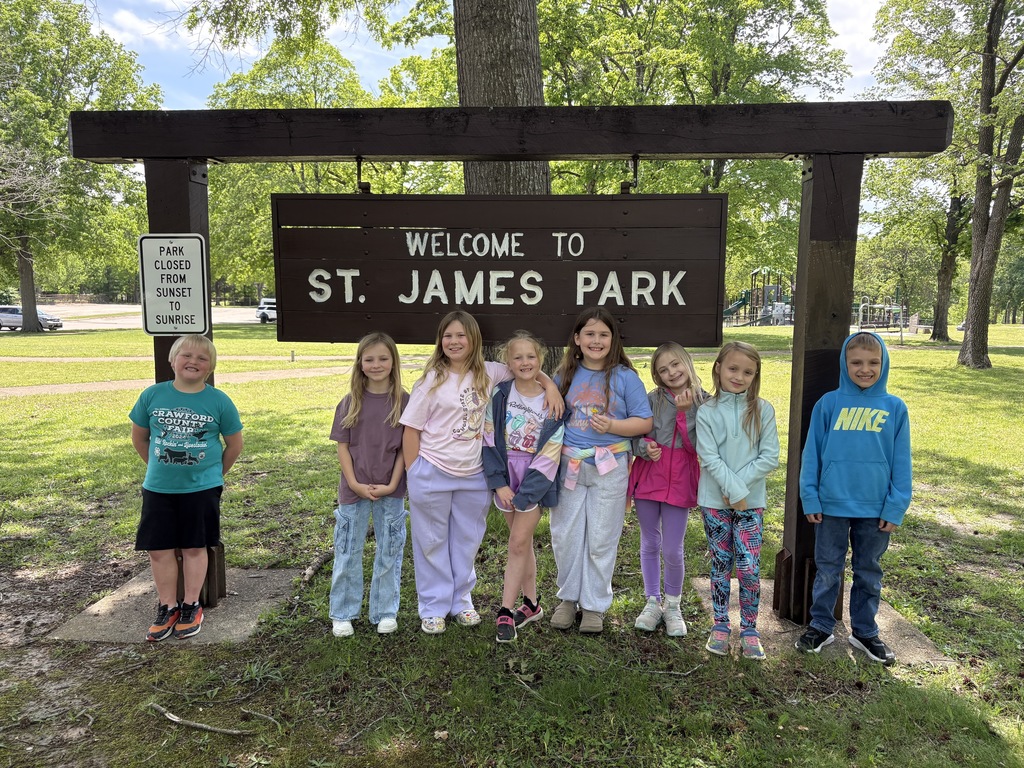 Children stand in front of a sign that reads "Welcome to St. James Park" on a sunny day.