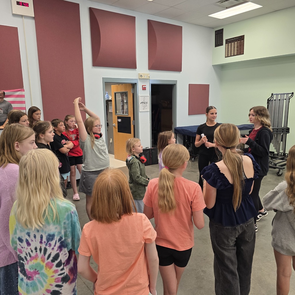 A group of children and two adults gather in a room, with the adults leading activities.