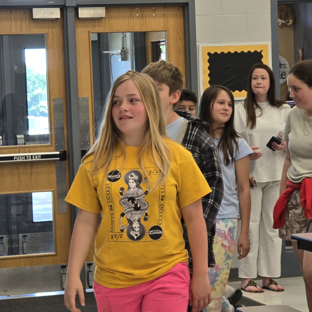 A group of students standing in a hallway. A girl in front wears a yellow shirt with graphics.