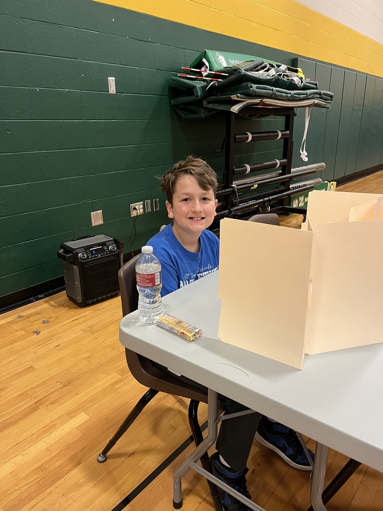 A young boy in a blue shirt sitting at a table with a water bottle.