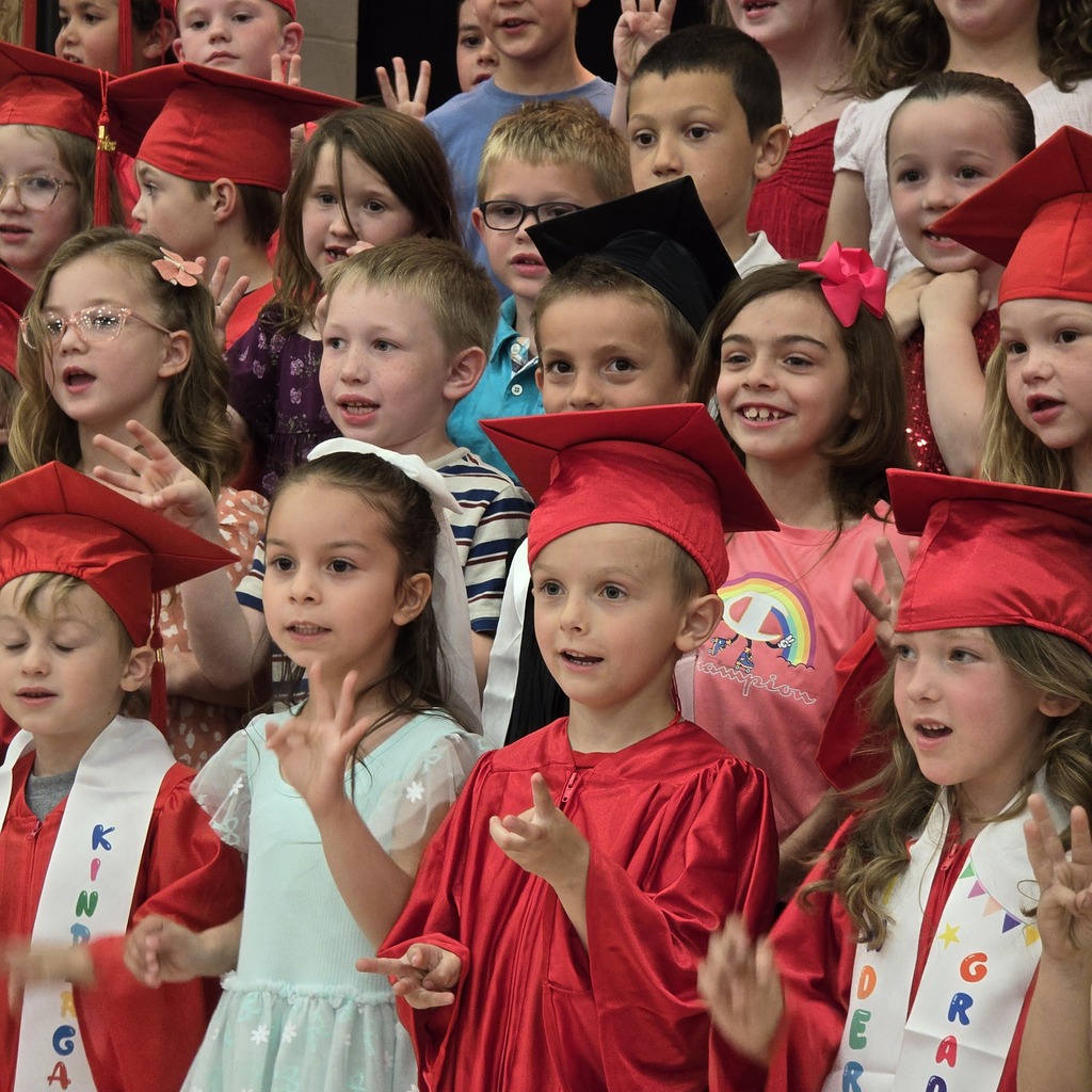 A group of kindergarten students wearing red graduation caps and sashes, with sashes that say "Kindergarten."
