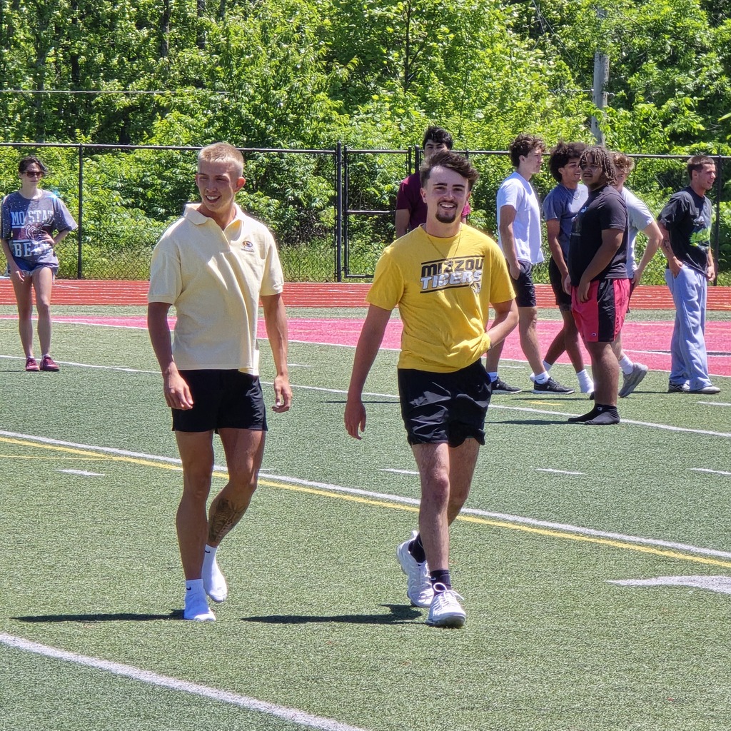 A group of people in athletic wear on a field with white markings and trees in the background.