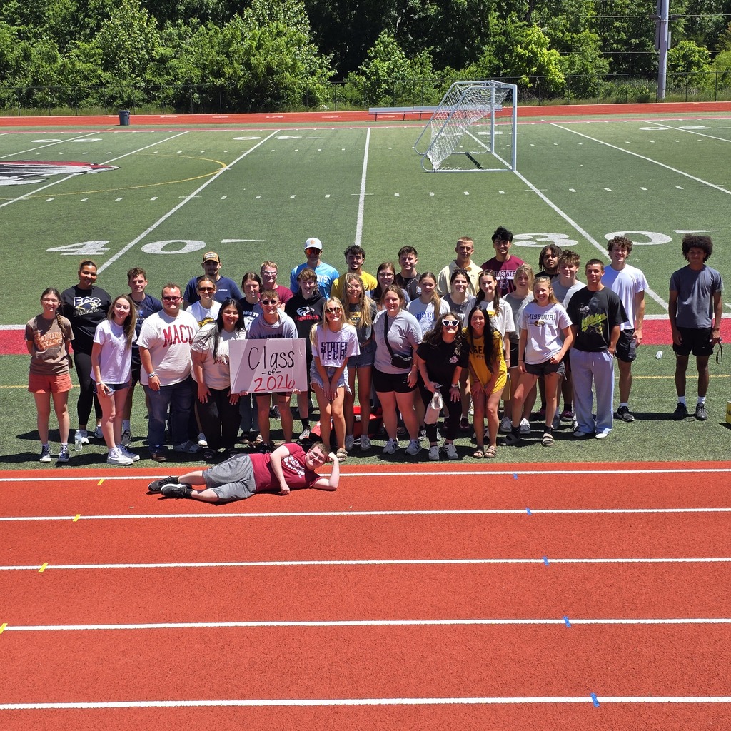 Group of people on a track, some standing and some kneeling. One person lying down holding a sign.