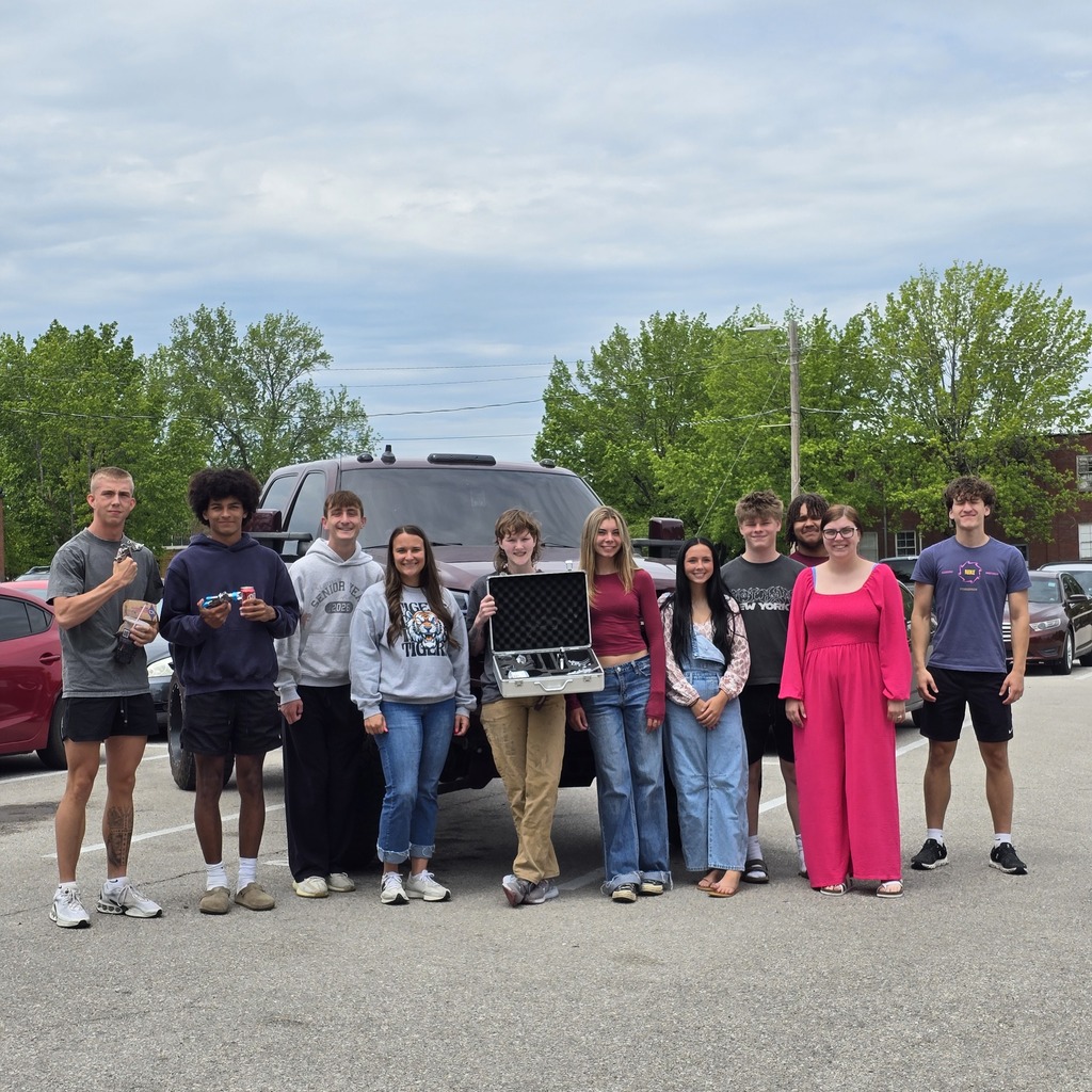 A group of students in various clothing poses for a picture in a parking lot.