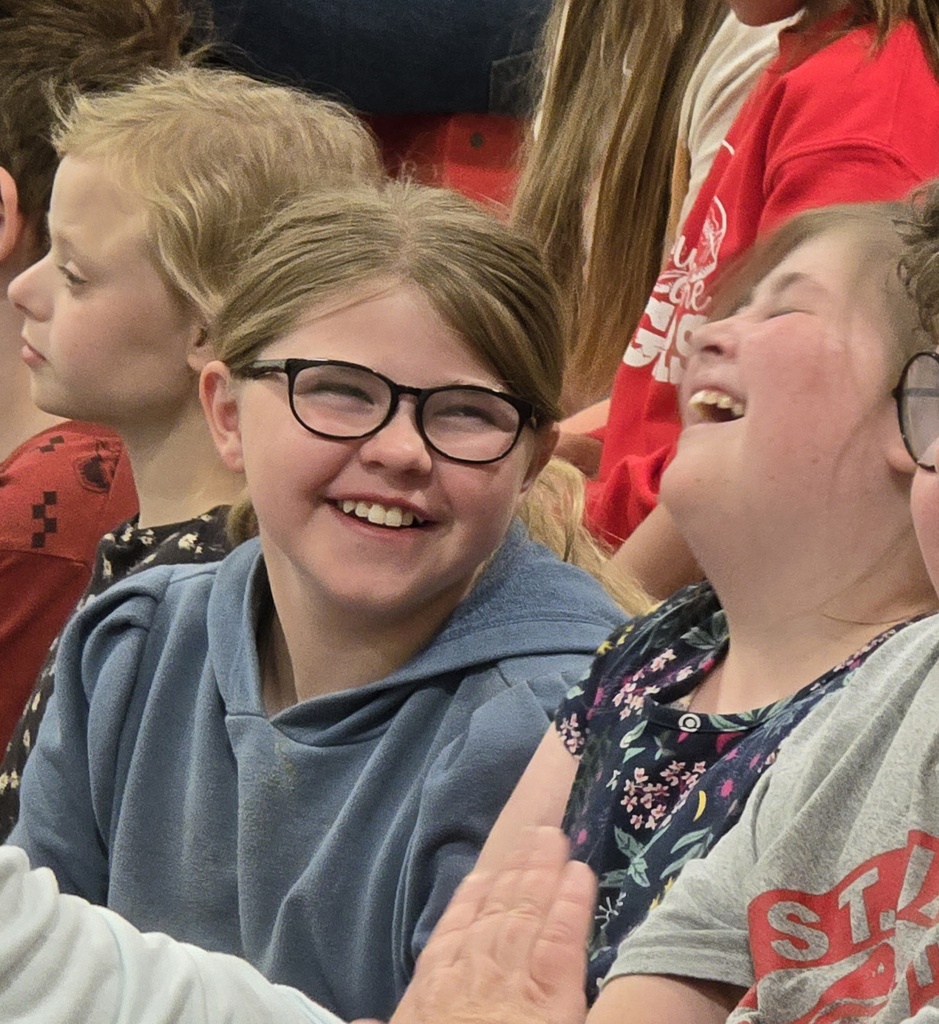 Several young children, some wearing glasses, smile and laugh. One child has a hoodie.