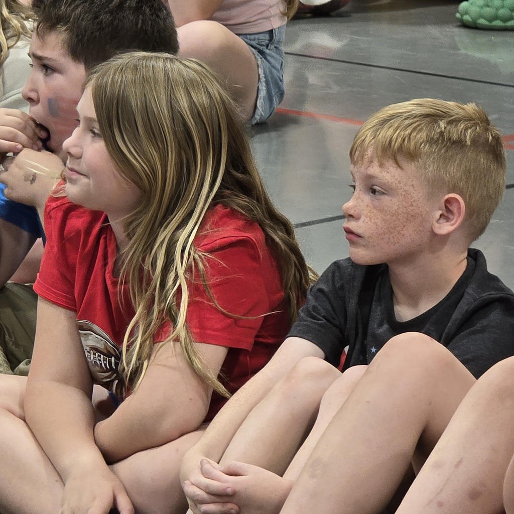 Four children, two girls and two boys, seated, facing forward, on a polished floor. Two have blond hair, two have brown hair.