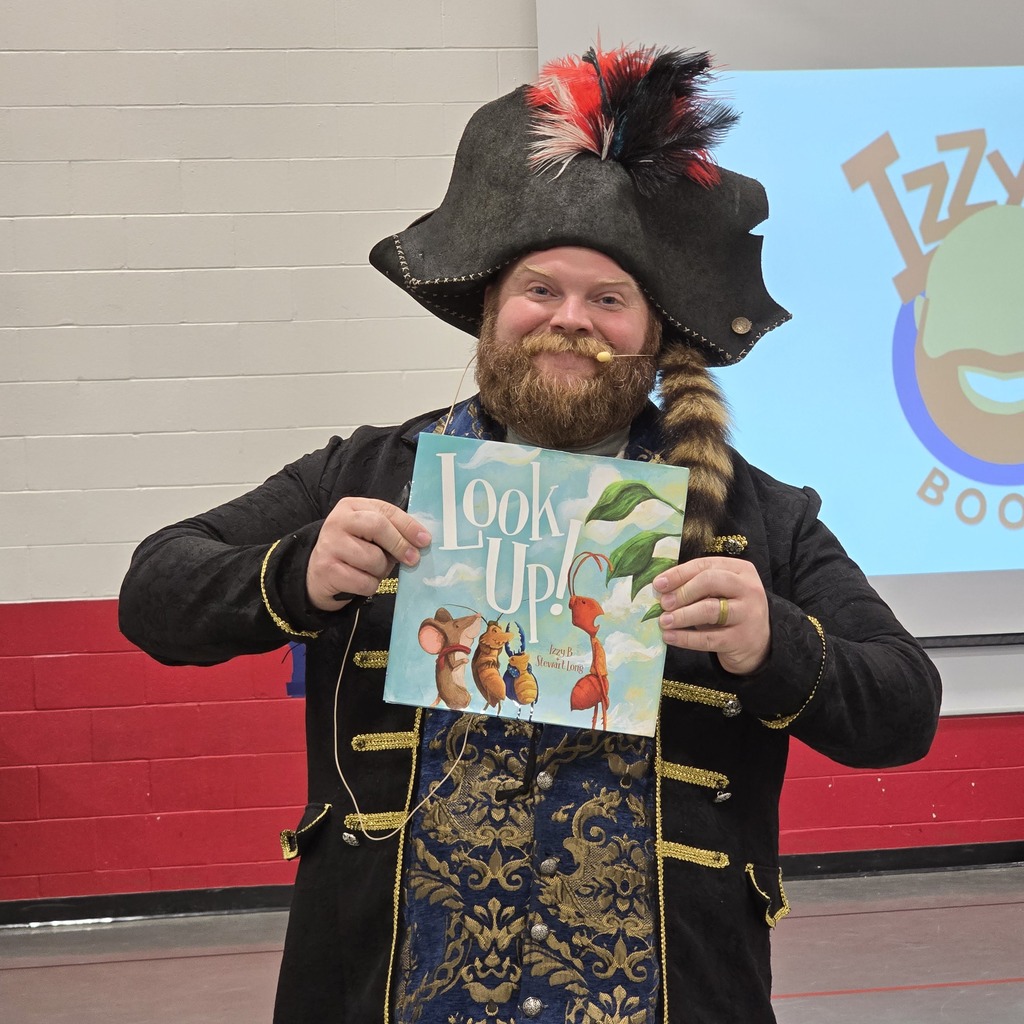A person in a pirate costume holds a book titled "Look Up!" in a room with red walls.