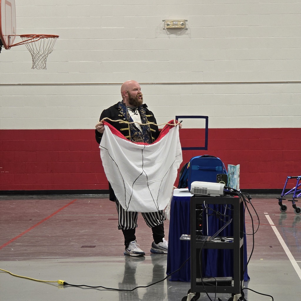 A person in costume holds a large cloth while standing in a gymnasium. A projector is set up on a table.
