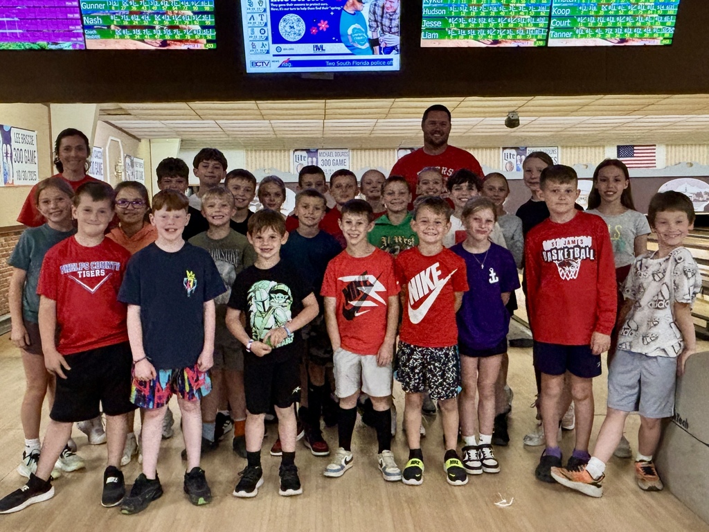 Children and an adult stand together in a bowling alley with bowling lanes and scoreboards.
