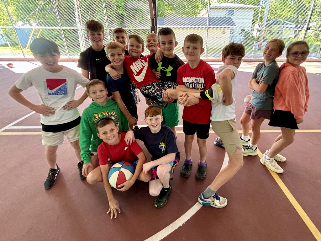 A group of kids pose for a photo on a basketball court. They are wearing different colored shirts.