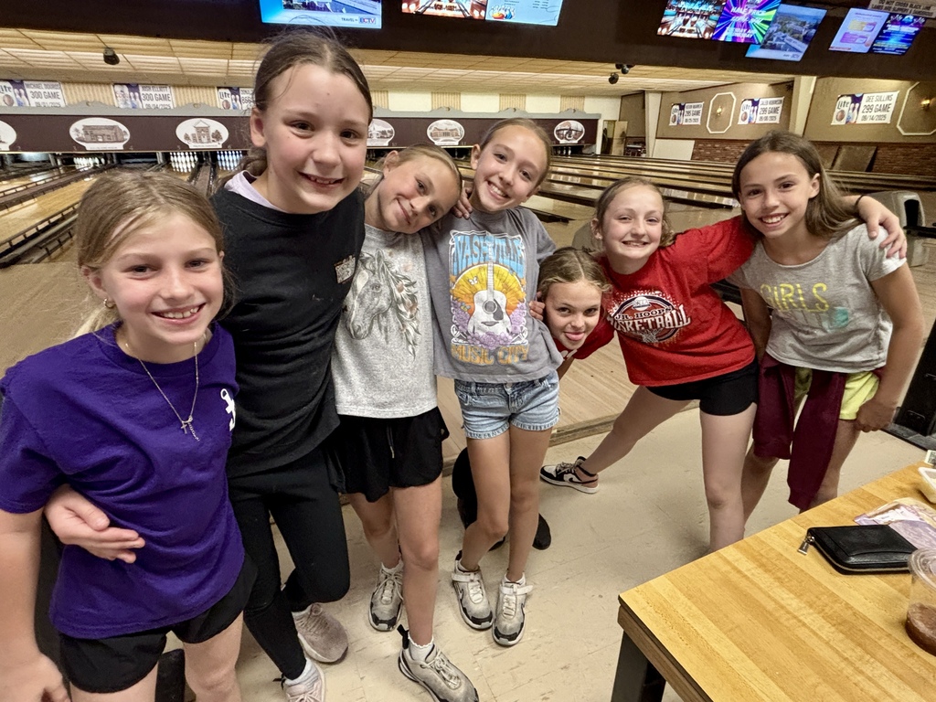 A group of girls in different colored tops and shorts pose for a photo in a bowling alley.