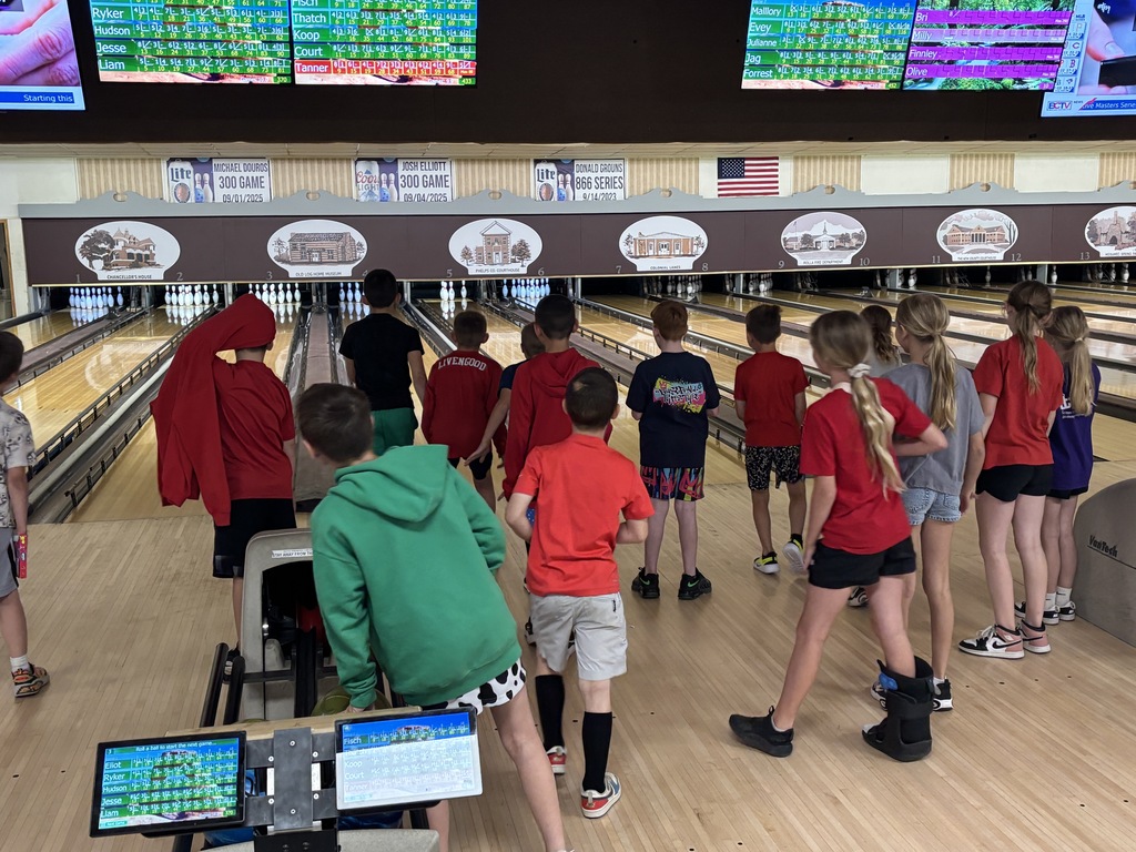 A group of children in matching shirts and shorts stand at bowling lanes, with screens showing scores in the background.