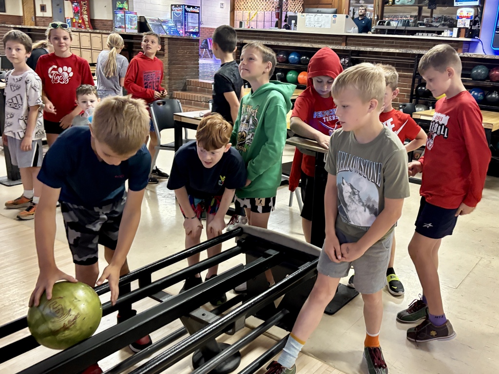 A group of children in a bowling alley, with one child holding a bowling ball and another on a lane.