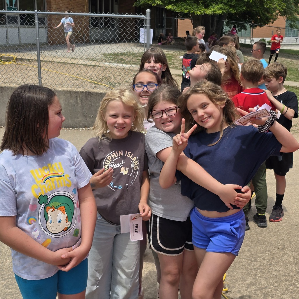 Children stand in a line at an outdoor school event, smiling and posing for the camera.