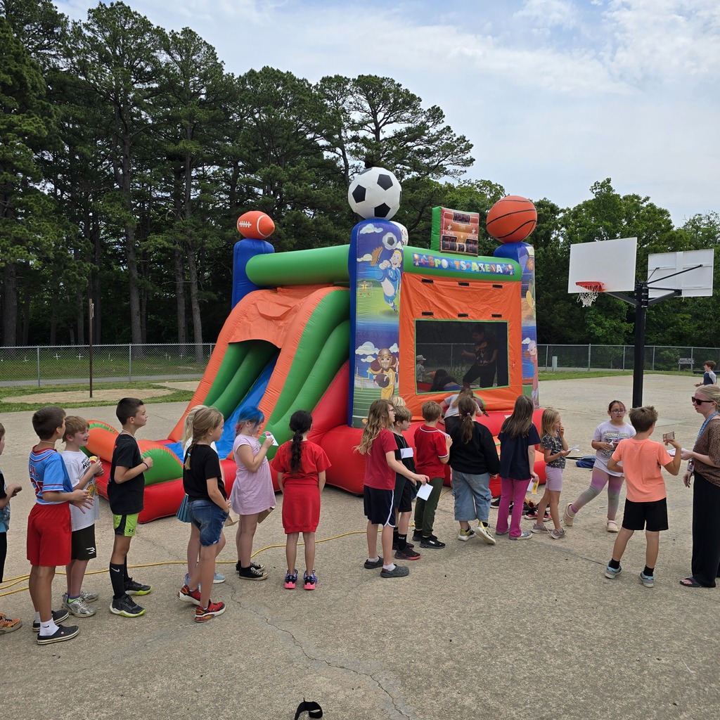 A group of children gathers around an inflatable sports bounce house, featuring soccer balls and basketballs.