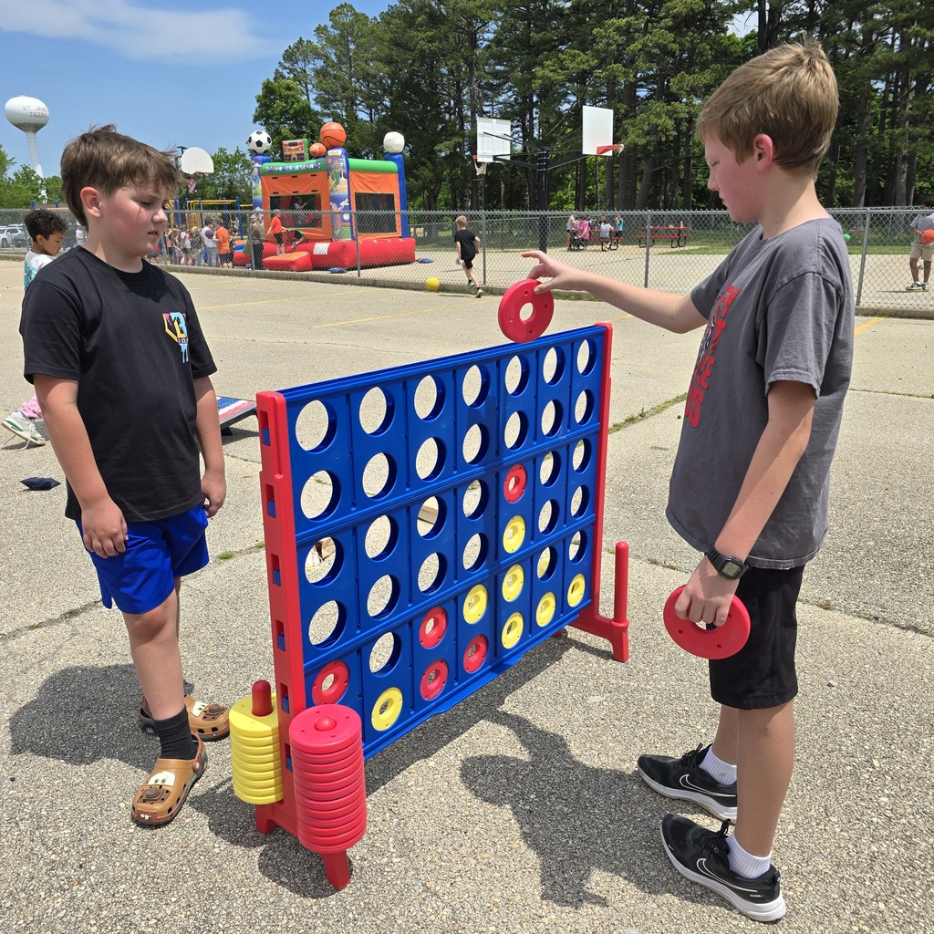 Two children play a game of Connect Four on a sunny day. One holds a red disc.