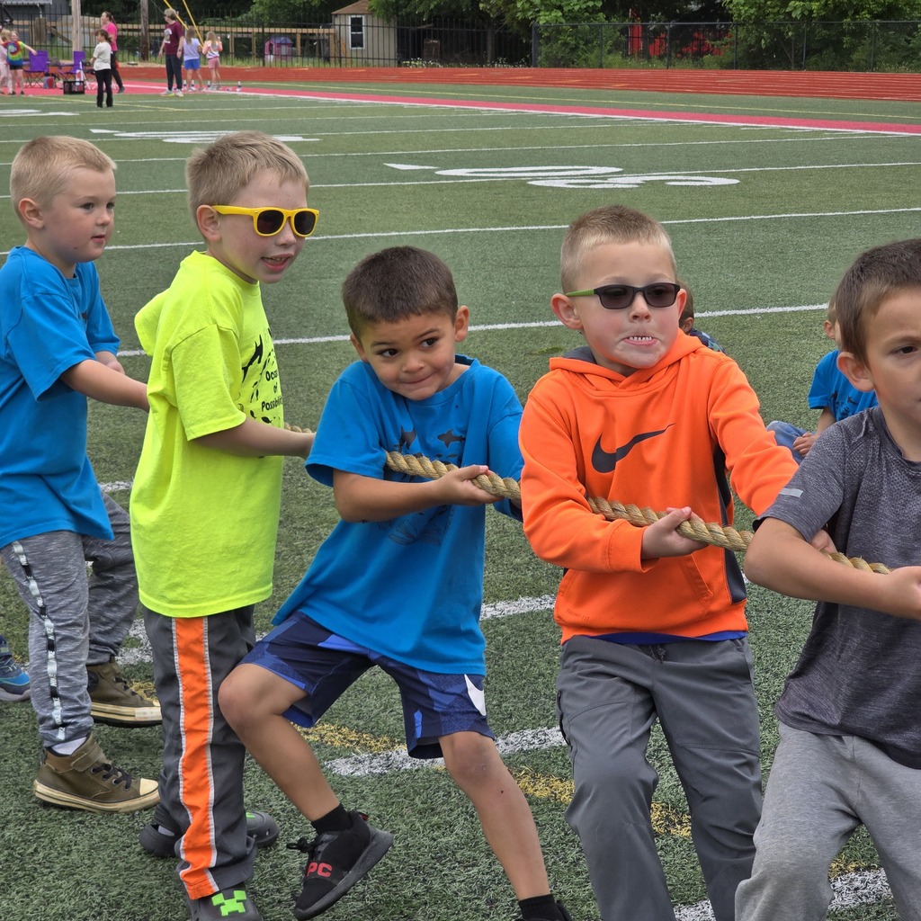 Five children with glasses and sneakers participate in a tug-of-war on a football field.