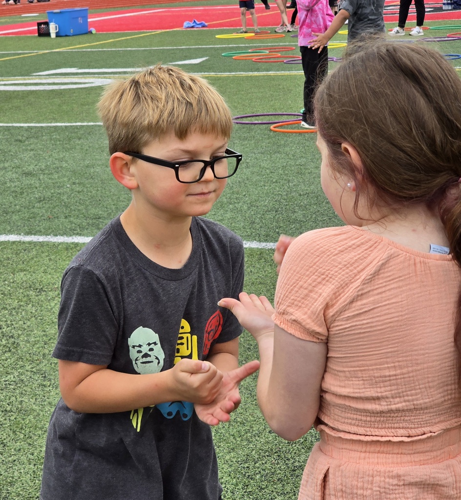 A boy and girl converse near a grassy field with white lines and hula hoops.