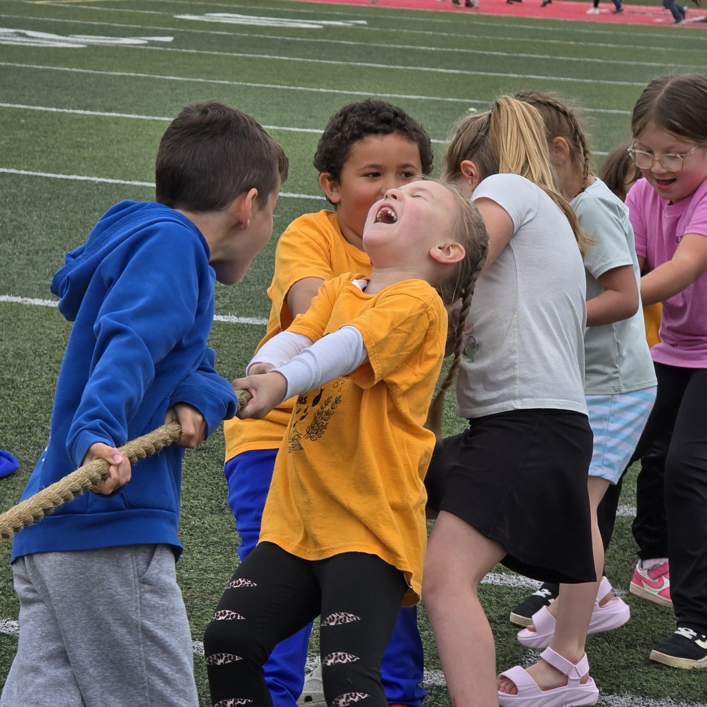 Kids playing tug-of-war on a football field. Four children are pulling on ropes, while two others watch.