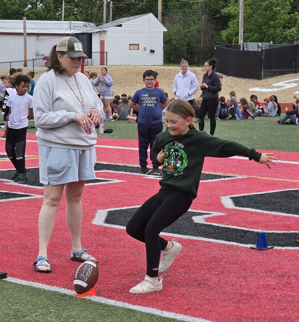 A woman and a girl playing kickball on a football field. The girl is kicking the ball.