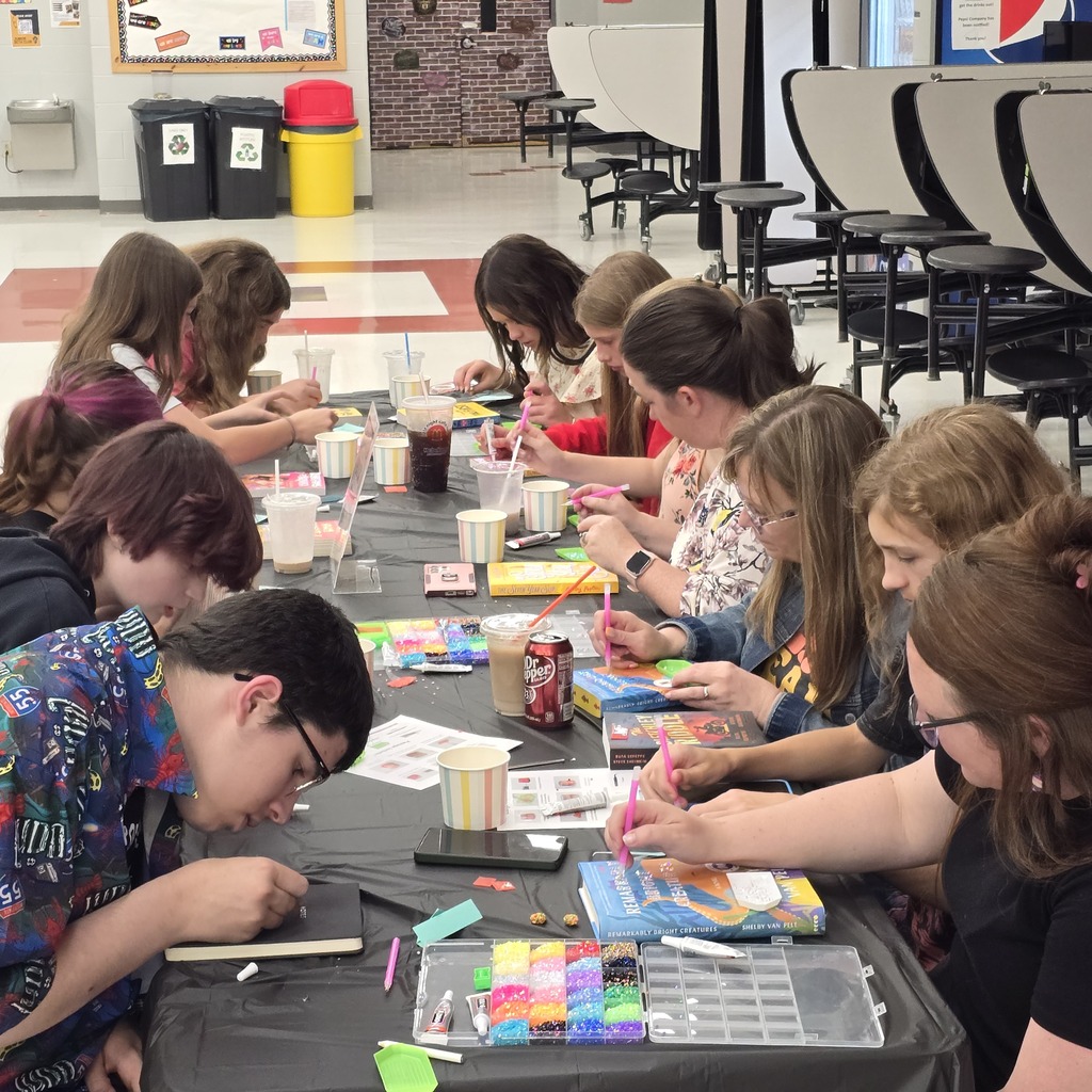 Several people in a room, seated around a long table covered in black cloth, engaging in coloring activity.