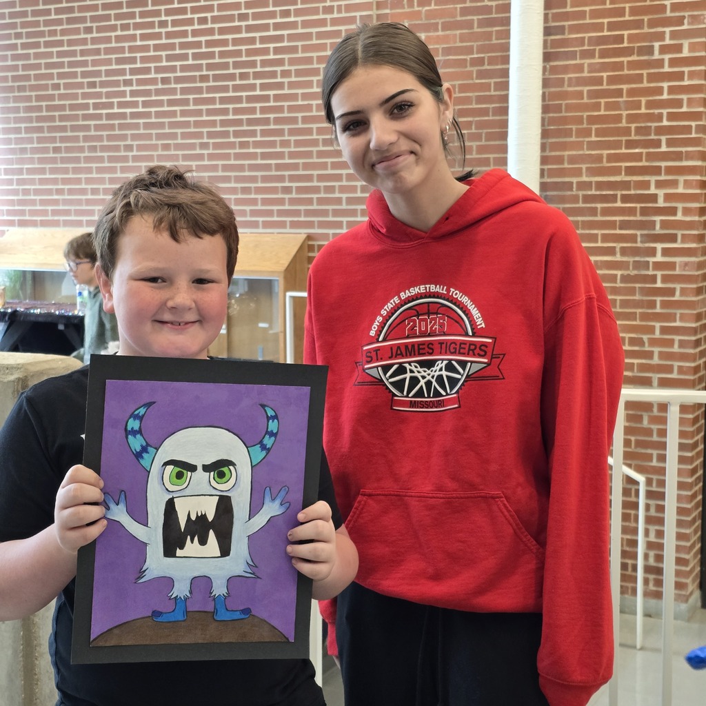 Two children, one holding a drawing of a monster, stand in front of a brick wall.
