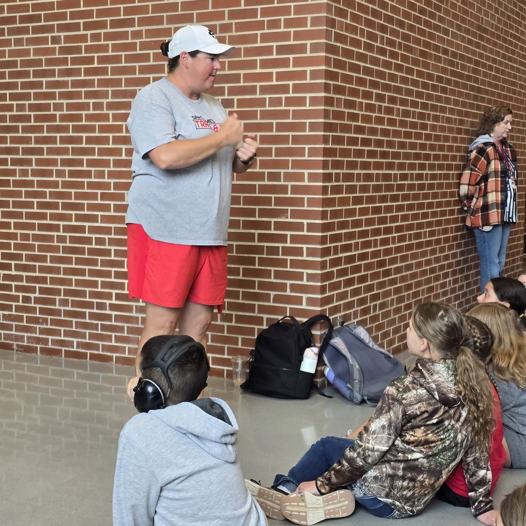 A group of people sit in a room with a brick wall; one person stands and speaks.
