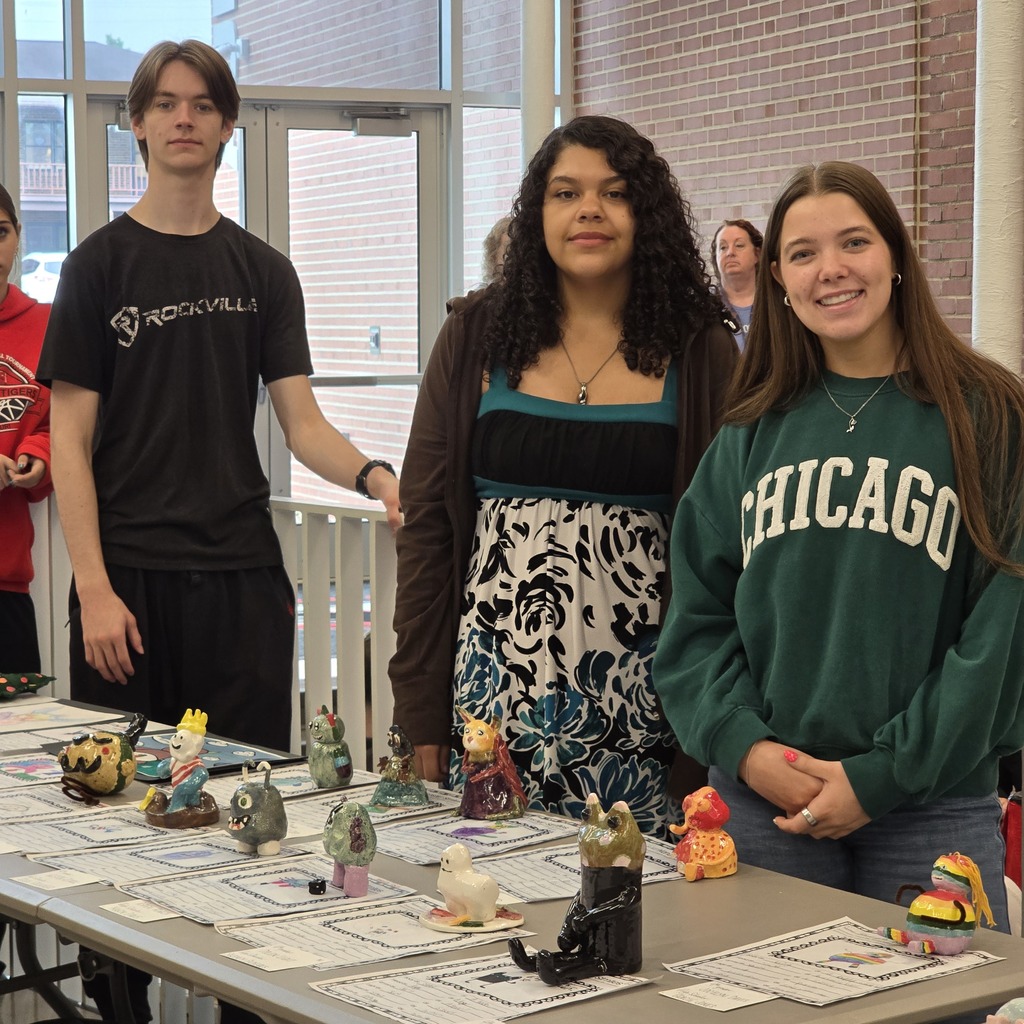 Four young people stand behind a table displaying miniature sculptures, with one wearing a black shirt and another a green Chicago sweater.