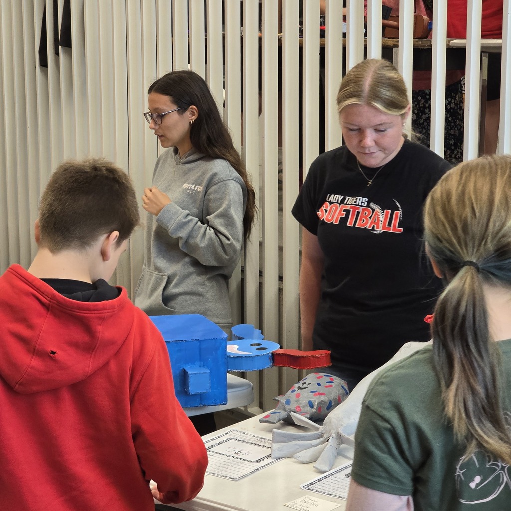 Four people at a table. A woman wearing a gray hoodie, a woman in a black t-shirt, a boy in a red hoodie, and a woman with a ponytail.