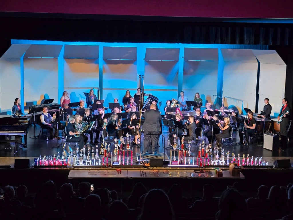 A band performs on a stage with blue lighting, in front of an audience seated in front.
