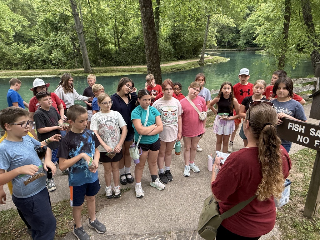A group of children and adults standing by a lake, with a sign reading "Fishing: No Fishing."