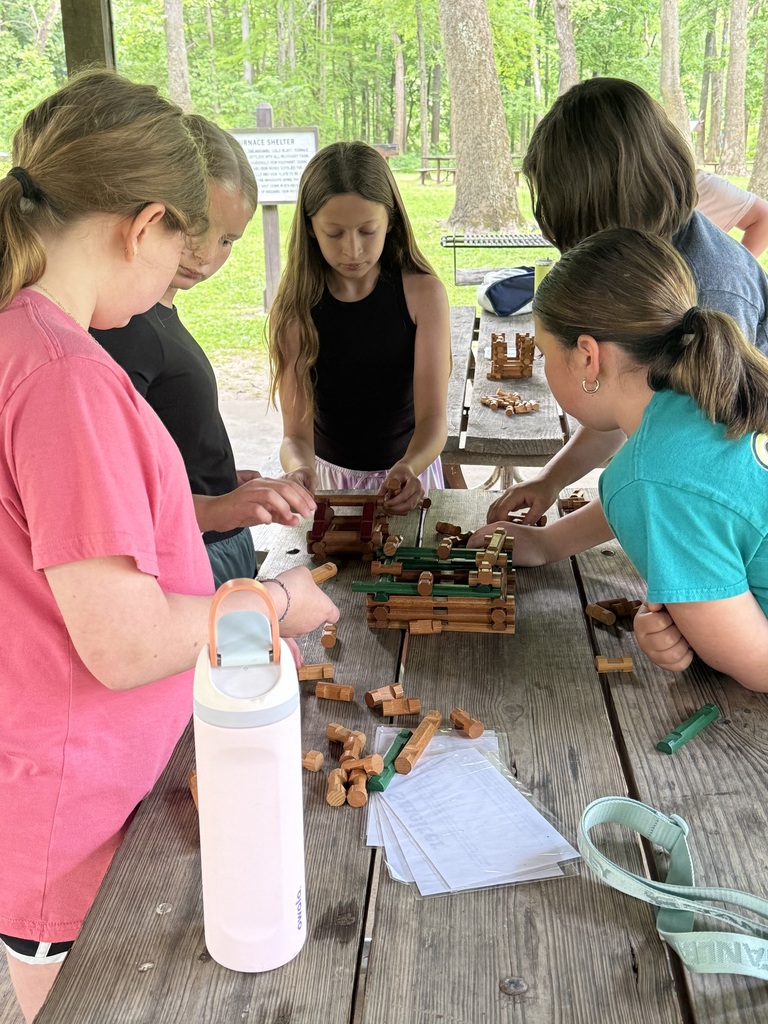 Six children are sitting at a picnic table, using building blocks. One of them is wearing glasses.