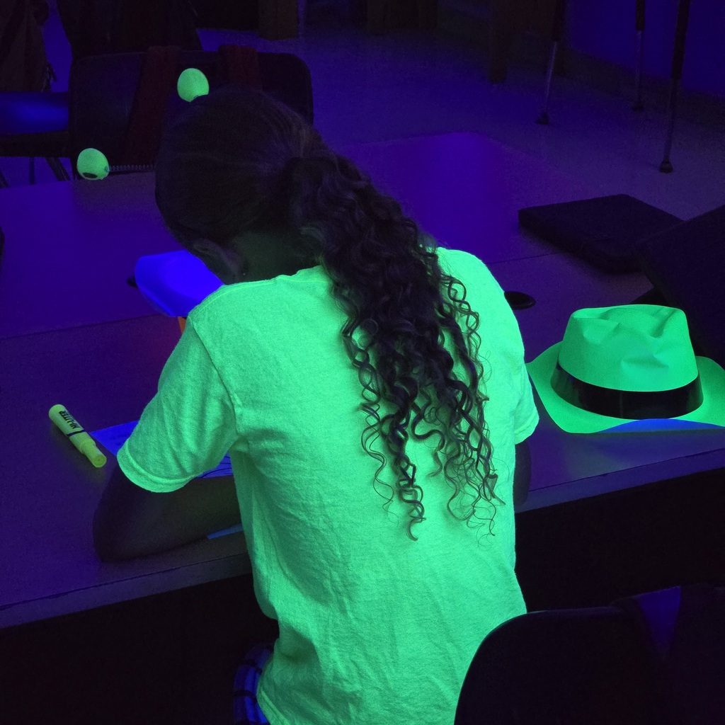 A person sits at a table in a room with a low-light setting and a green glow on their shirt.