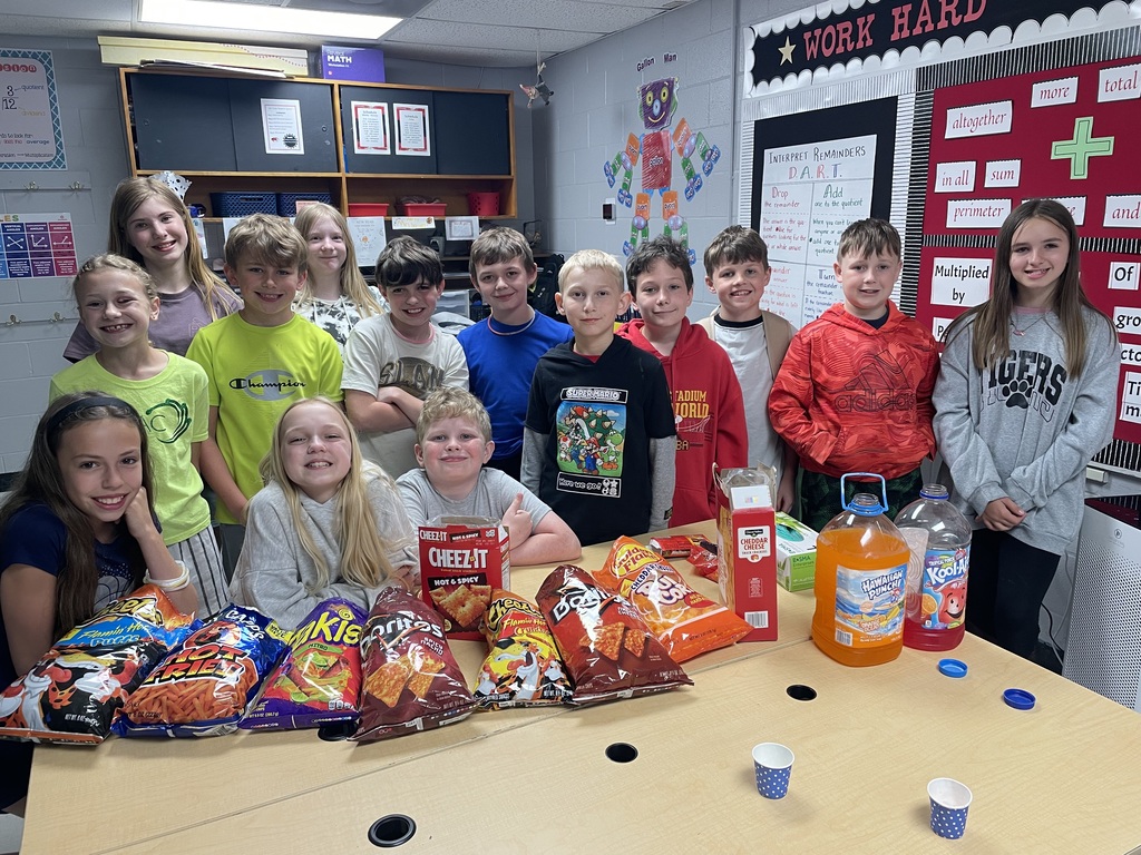 A classroom setting with children gathered around a table filled with snacks and beverages.