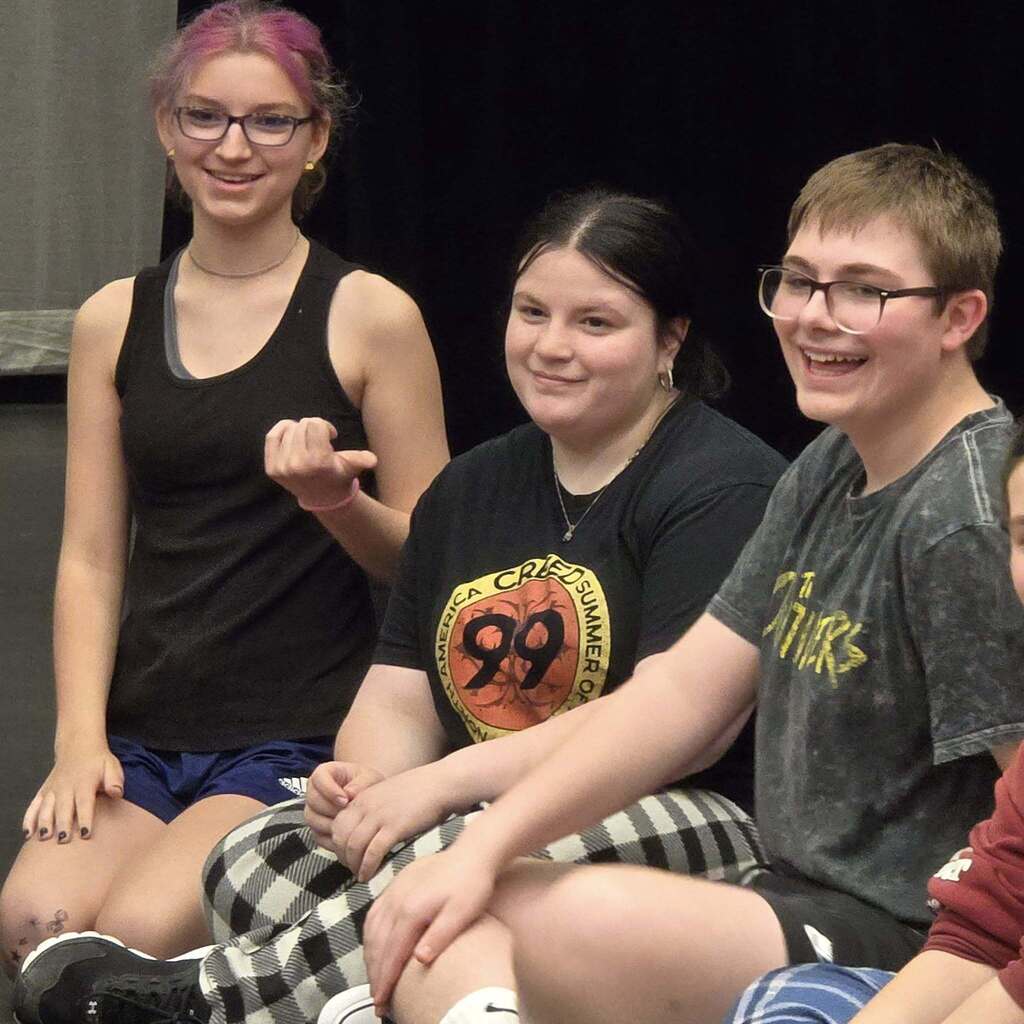 Four students, with one girl wearing pink hair, sitting and smiling in a row.
