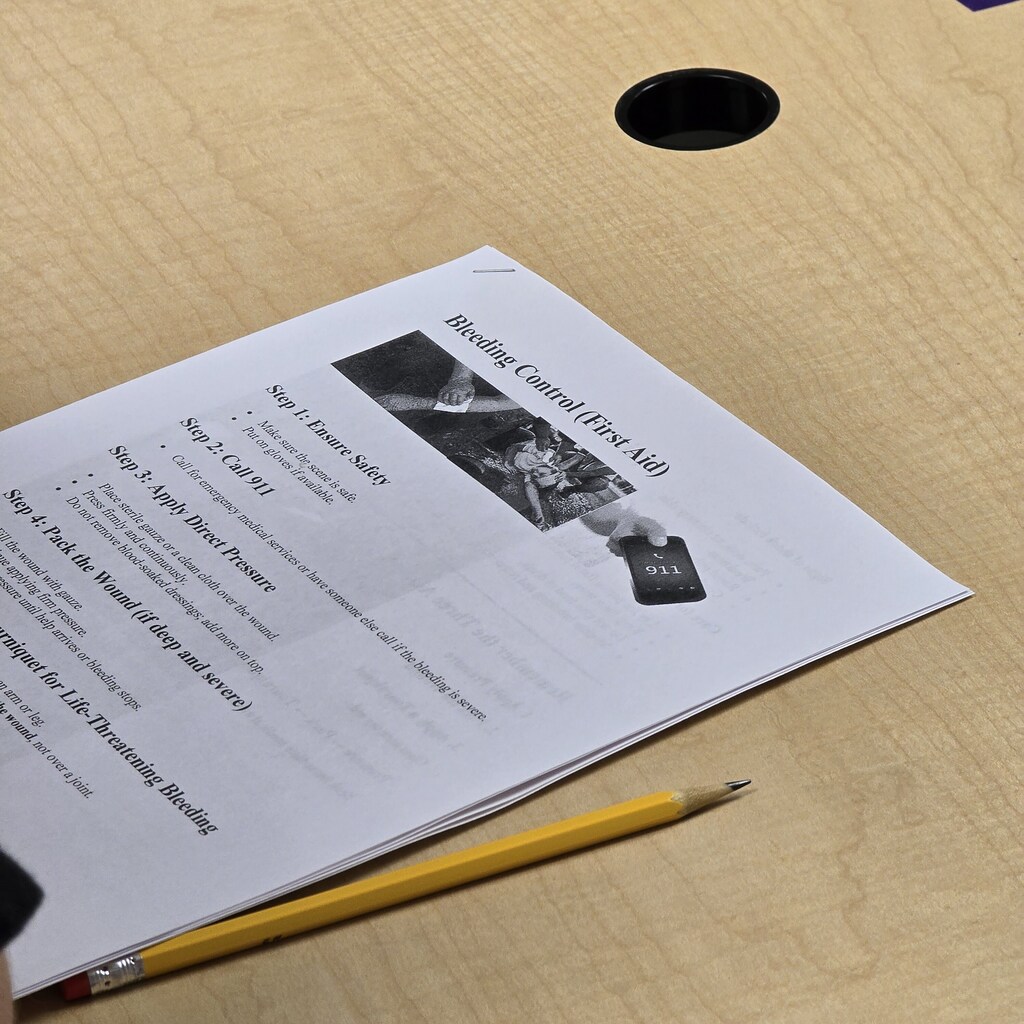 A document titled "Bleeding Control at Work" lies on a table, partially covered by a yellow pencil.