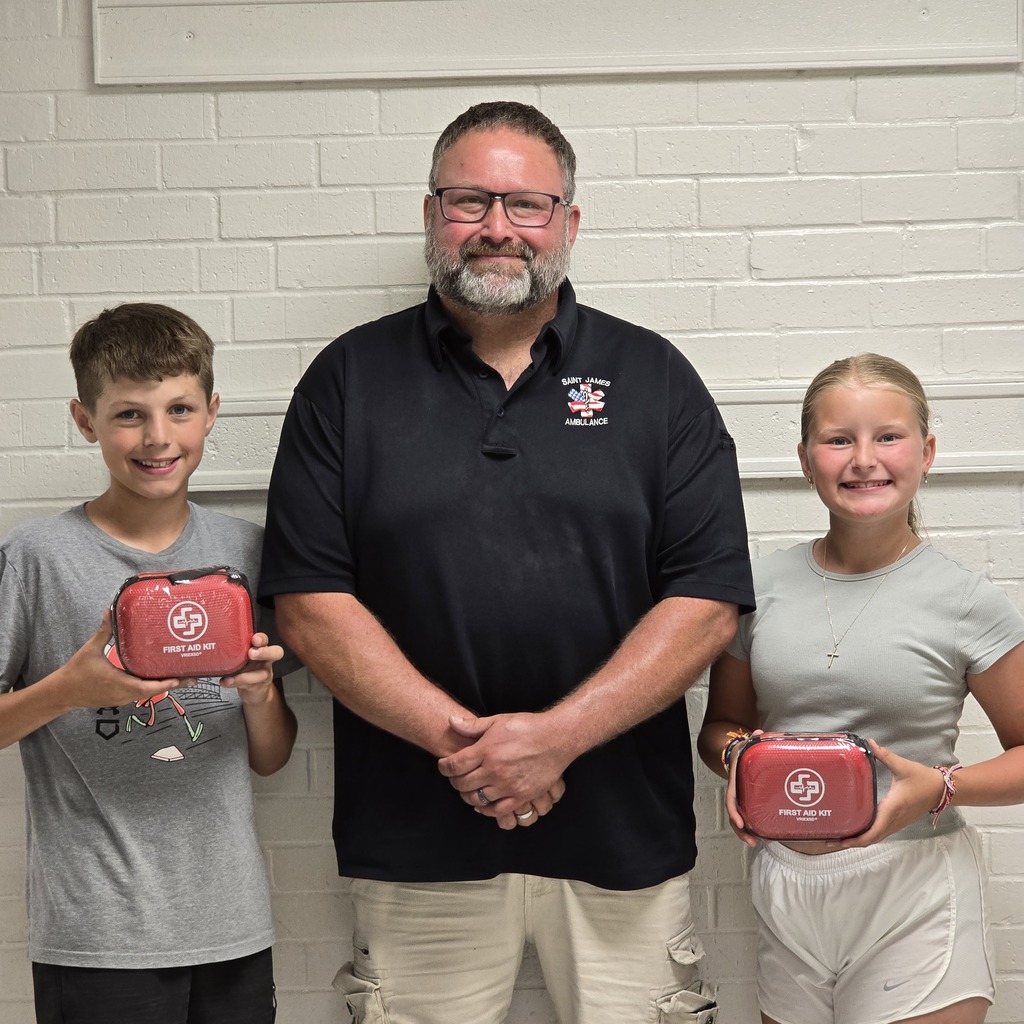 A man and two children hold red emergency kits, posing for a picture against a white brick wall.
