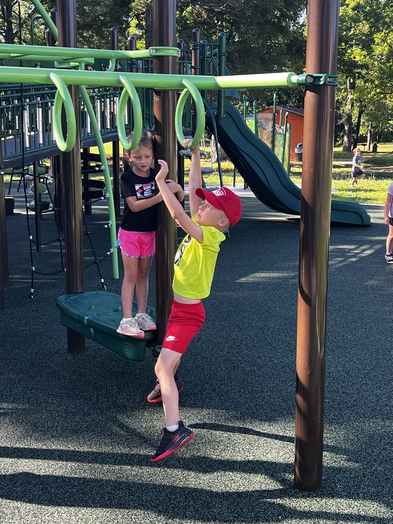 Two children play in a playground. One climbs rings while the other stands nearby. A slide is behind them.