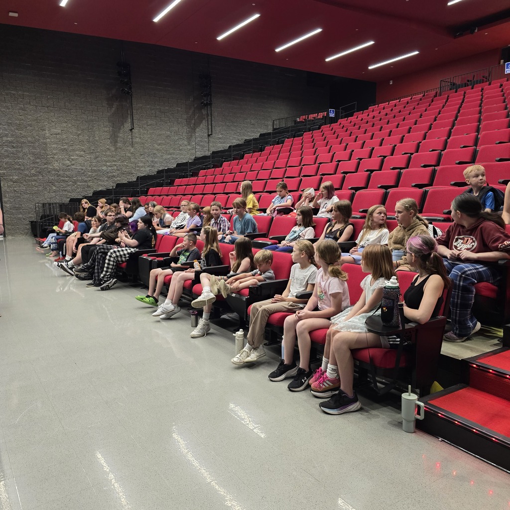 Theater with red chairs. Some people are sitting in rows, and others are standing.