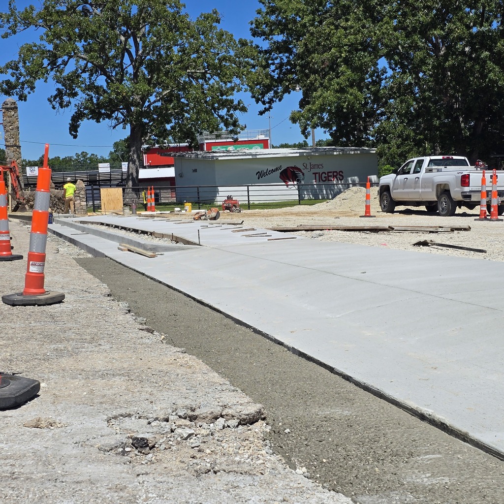 Construction site with new pavement and orange traffic cones. A white pickup truck is parked nearby.