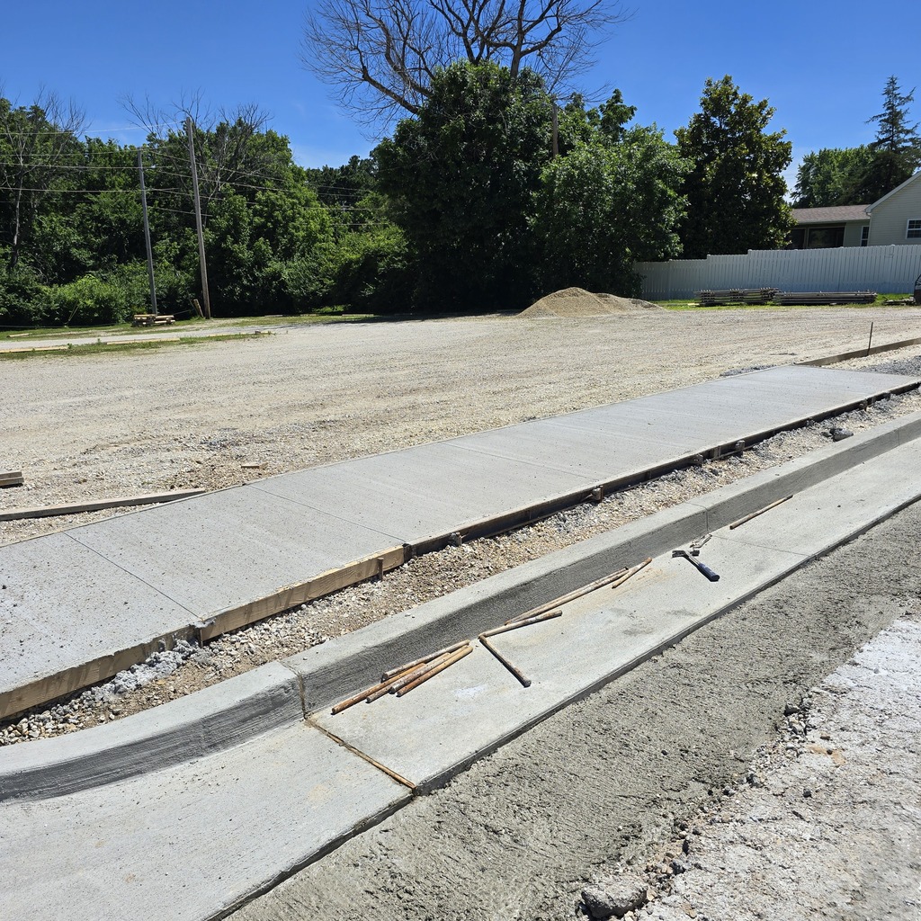 A sidewalk is under construction with exposed tools and dirt. A dirt area is in the background.