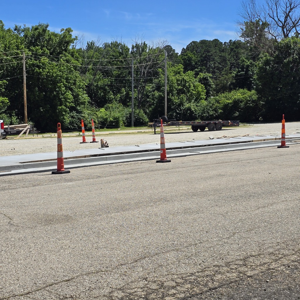 Empty road with traffic cones and construction equipment. Trees and greenery visible in the background.