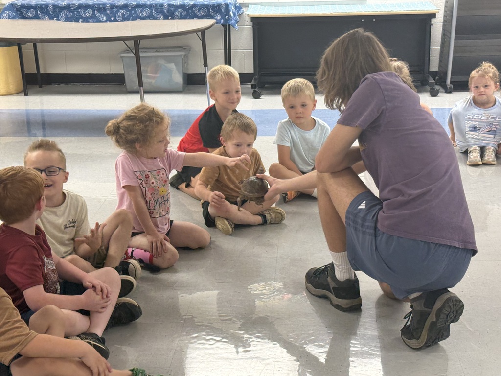 A group of children sit in a circle on the floor, listening to an adult who holds a small animal.
