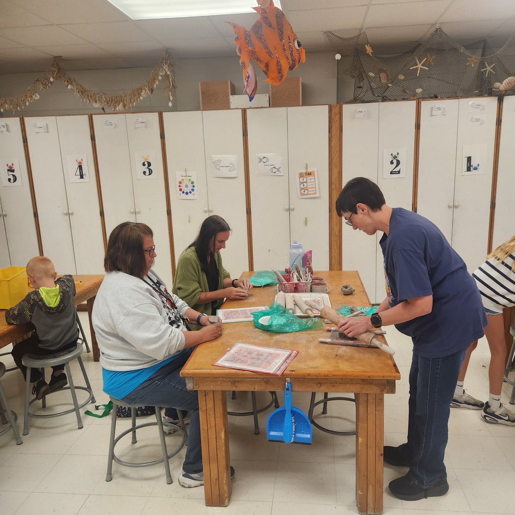 Group of adults and children around a table in a classroom with lockers in the background.