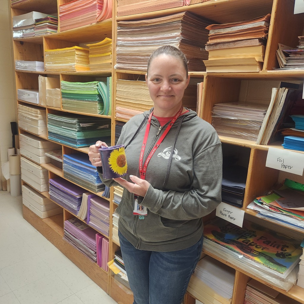 Woman with gray sweatshirt holding yellow sun design against background of stacked shelves with colorful paper.