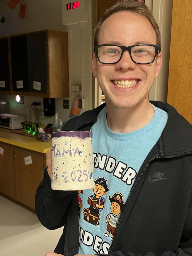 A person with glasses and a blue shirt holds a cup saying "Mama's 2025" in a kitchen.