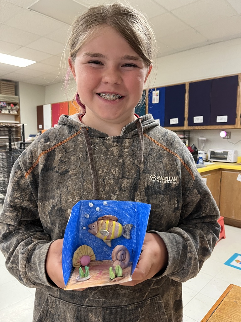 A child holding a small 3D art project of a fish and coral in a blue background.