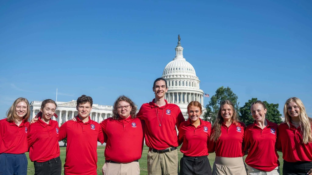 A group of people in red shirts and khaki pants stands in front of the Capitol building.