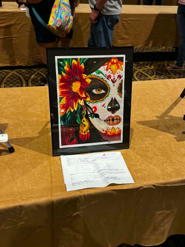 Framed artwork of a woman with flowers, skulls, and other designs on her face displayed on a table.