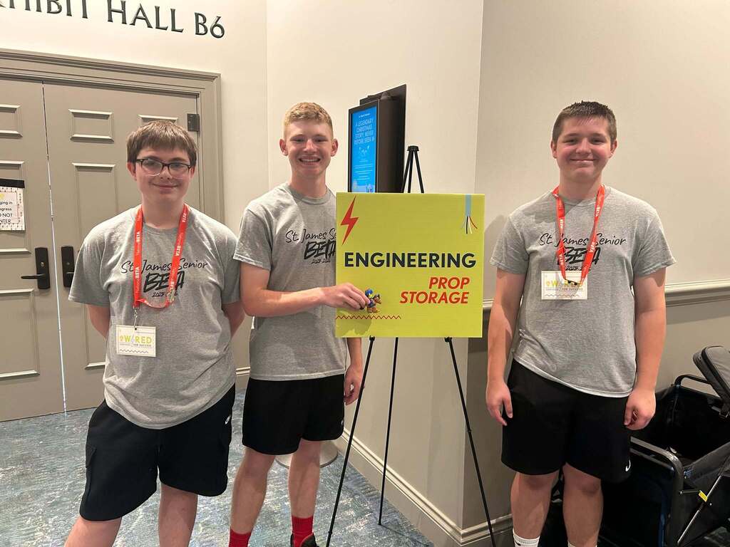 Three young men in matching gray shirts and black shorts pose with a sign reading "Engineering Pop Storage".